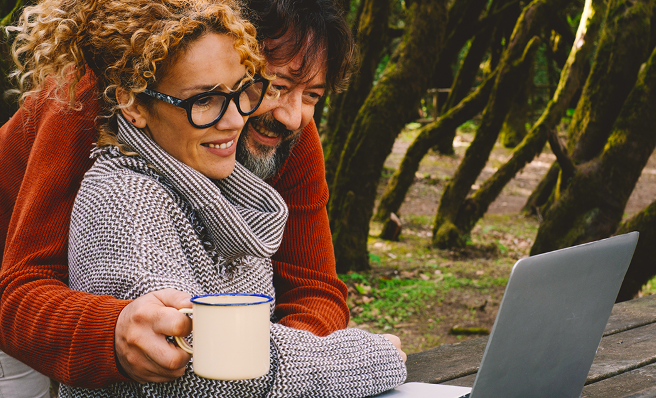 A man wraps his arm around a woman as they gaze at an open laptop together.