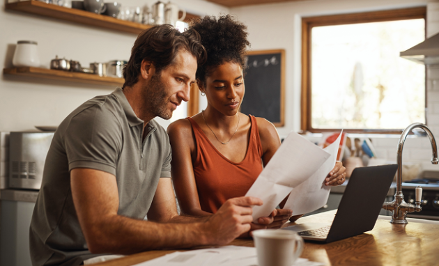 A man and woman review financial statements together in their kitchen.